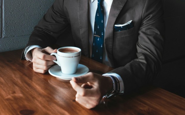 man holding cup filled with coffee on table